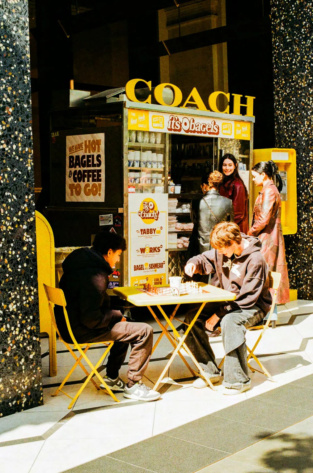 Customers at the Coach × It's Bagels cart, with chess table